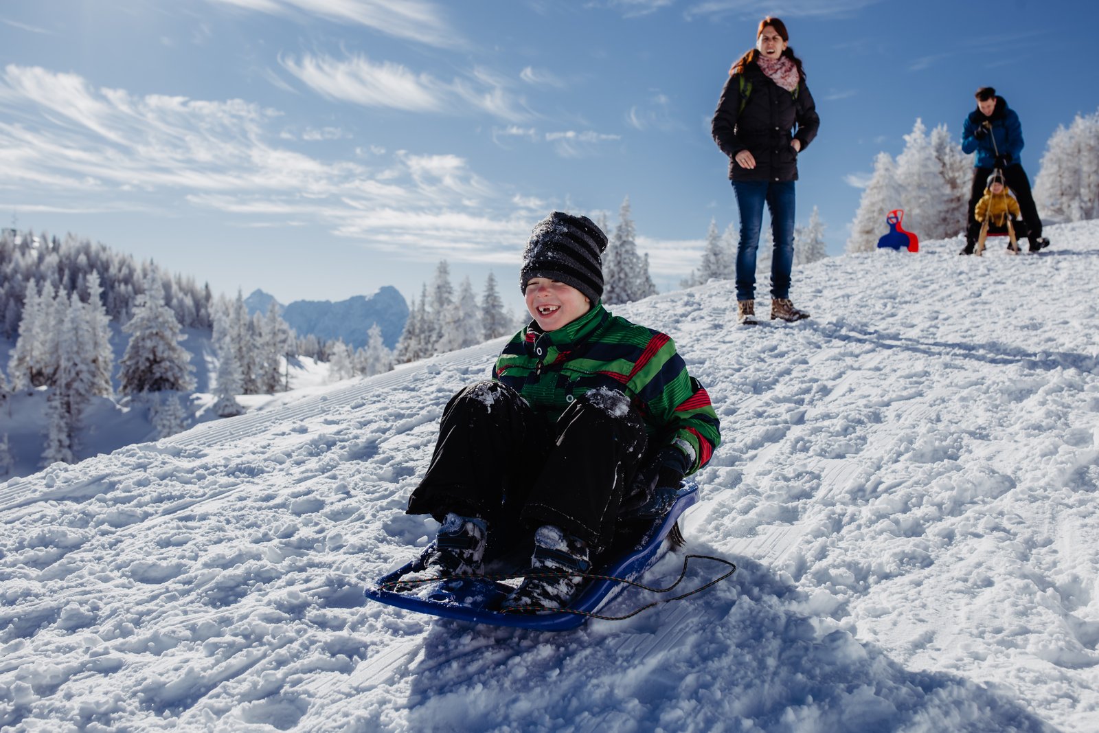 Ein Junge sitzt auf einem Schlitten am verschneiten Hang.