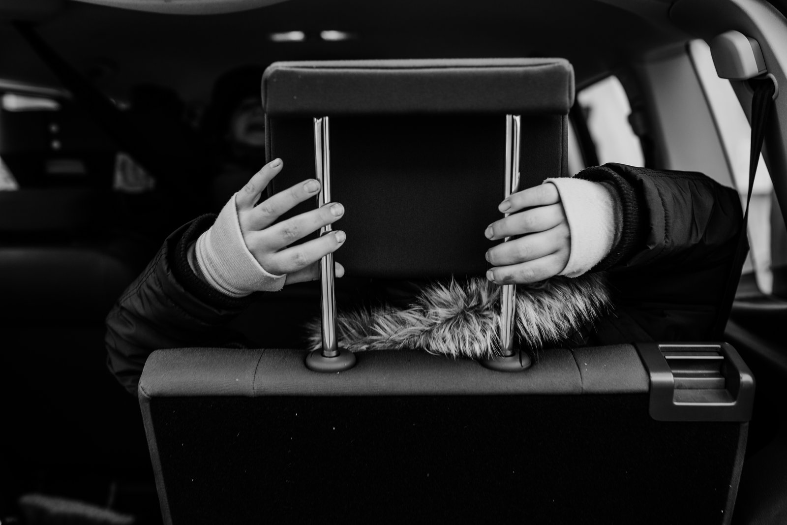 Kinderhände halten die Kopfstütze eines Autositzes, Schwarzweißaufnahme.