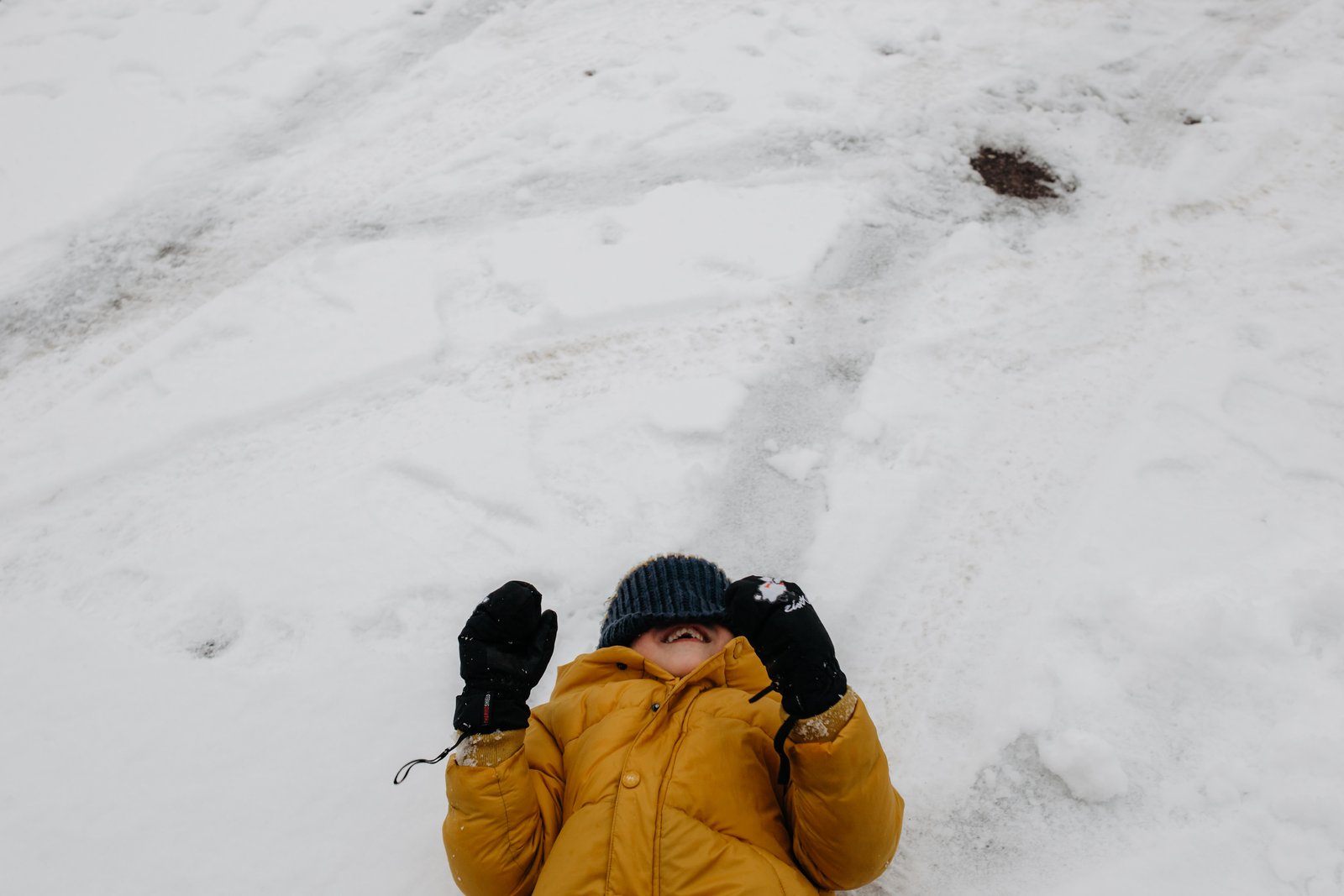 Ein Kind im gelben Wintermantel liegt im Schnee.