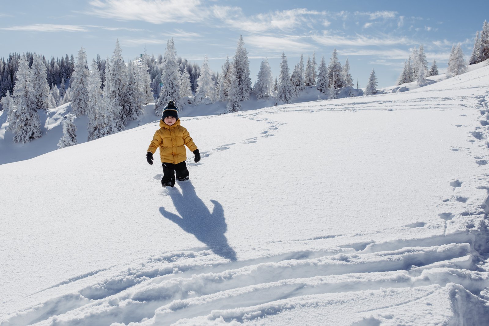 Ein Junge im gelben Wintermantel steht ruhig im weiten Schnee.