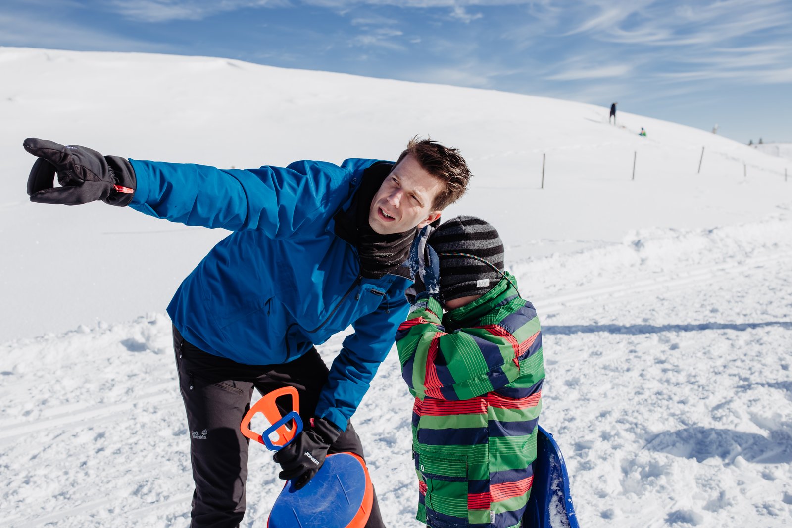 Ein Vater und sein Sohn zeigen lachend in die Schneelandschaft.