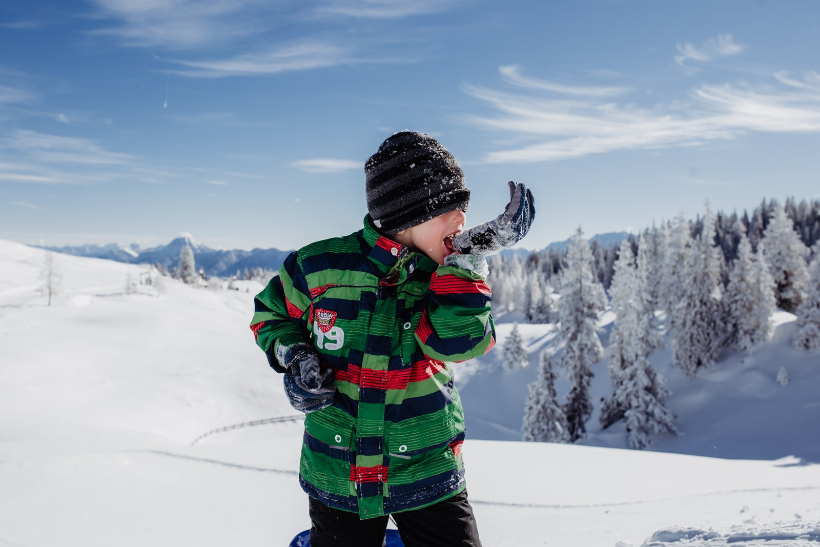 Ein Junge im grünen Wintermantel gestikuliert vor verschneiten Bäumen.
