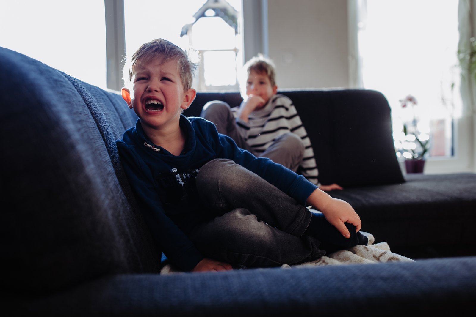 Ein weinender Junge sitzt auf dem Sofa, sein Bruder ist im Hintergrund.